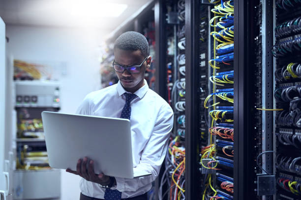 Cropped shot of a IT technician working on his laptop while standing inside of a server room